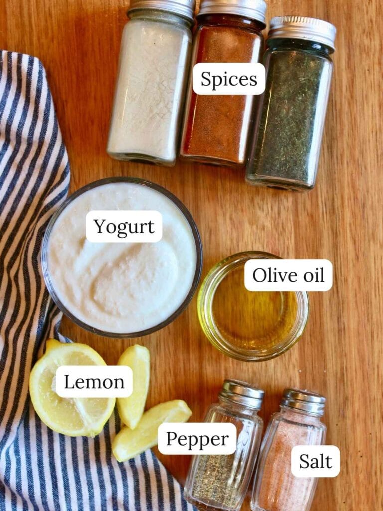 Ingredients for yogurt dill sauce including a lemon, spices, and olive oil on a wooden background.