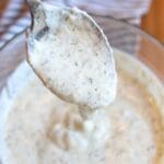 Closeup of yogurt dill sauce pouring off of a spoon into a bowl of the sauce.