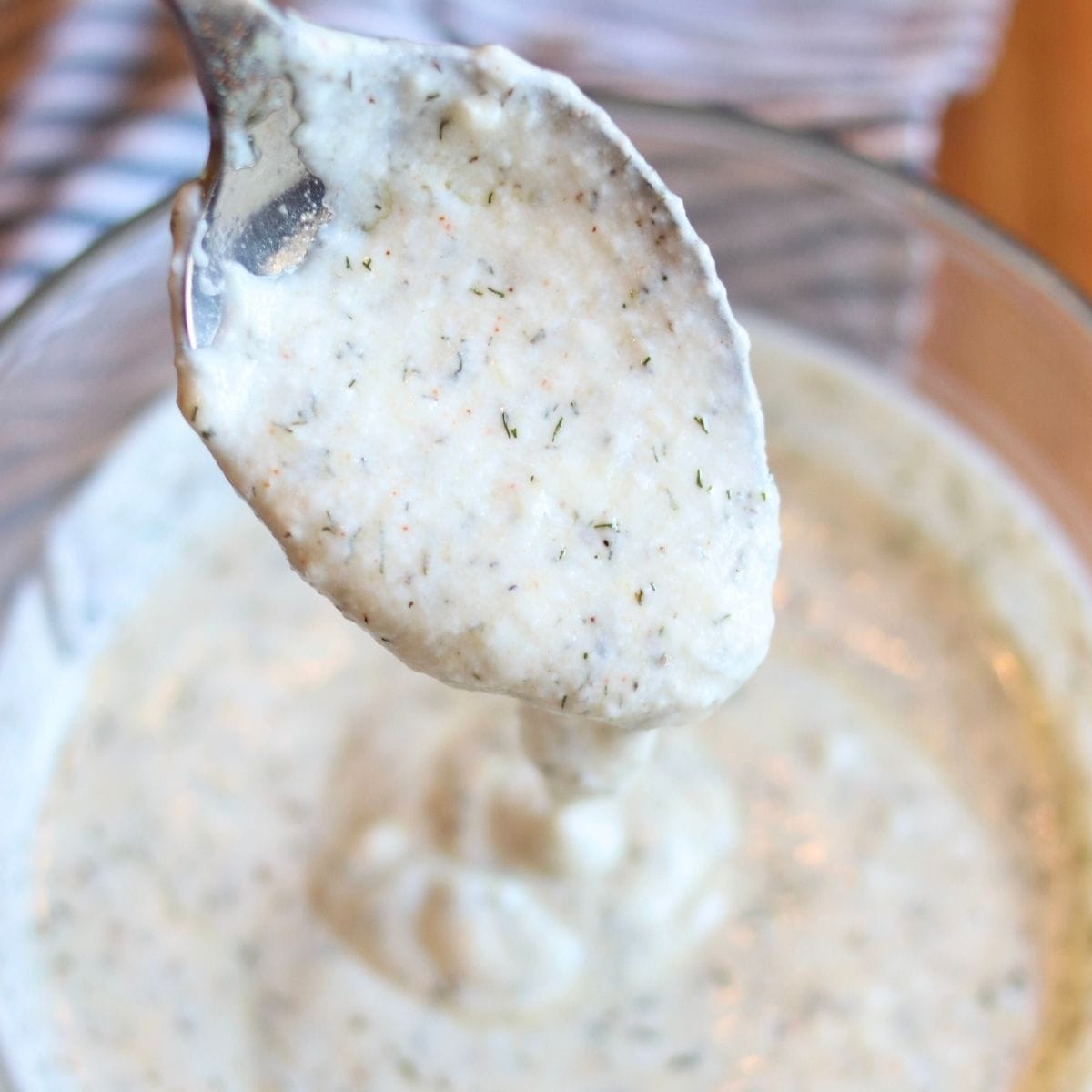 Closeup of yogurt dill sauce pouring off of a spoon into a bowl of the sauce.