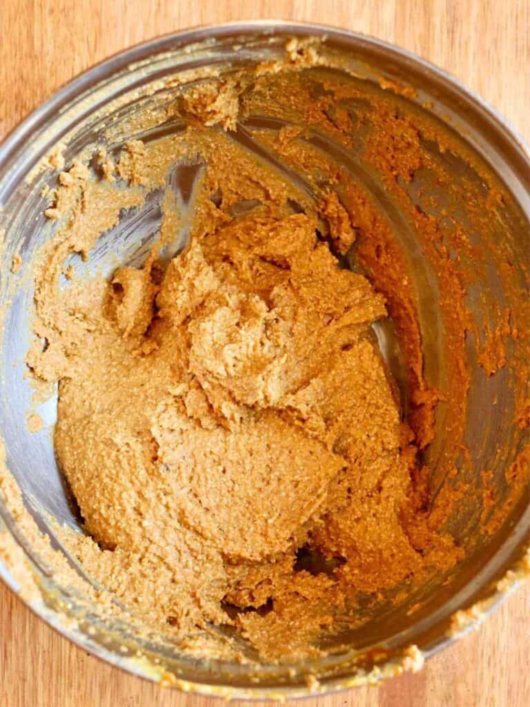 Bowl with thick, creamy brown gluten-free pumpkin cookie dough against a wooden backdrop, conveying a warm, homemade, and inviting feel.