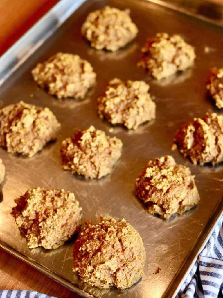 Twelve freshly baked, golden-brown gluten-free pumpkin cookies on a metal baking sheet. The background includes a striped cloth for a cozy, homemade feel.