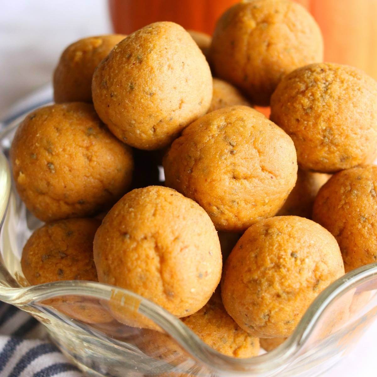 A glass bowl filled with round, golden-brown pumpkin protein balls. The texture appears soft and slightly speckled, suggesting a delicious, healthy snack.