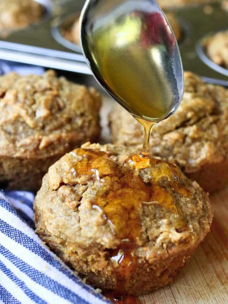 Close-up of freshly baked apple oat muffin being drizzled with honey, highlighting moist texture and wholesome ingredients.