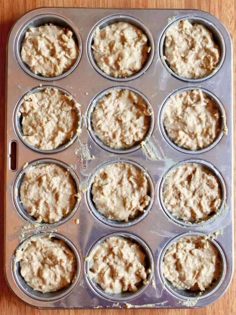 Overhead view of apple oat muffin batter evenly distributed in a 12-cup stainless steel muffin tin, ready for baking.
