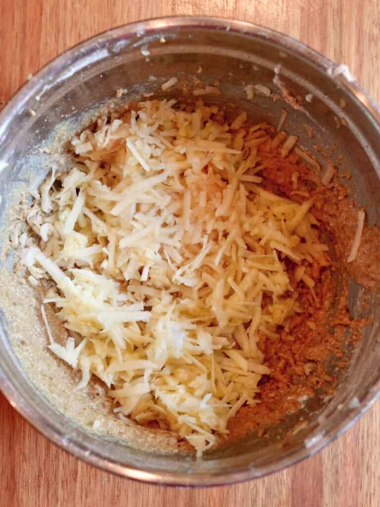 Grated fresh apples being folded into apple oat muffin batter in a mixing bowl on a wooden surface.