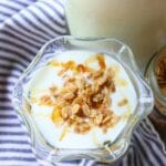 A glass dish of rich and creamy goat yogurt topped with granola and drizzled with honey. The setting is bright and inviting, evoking a fresh, healthy breakfast.
