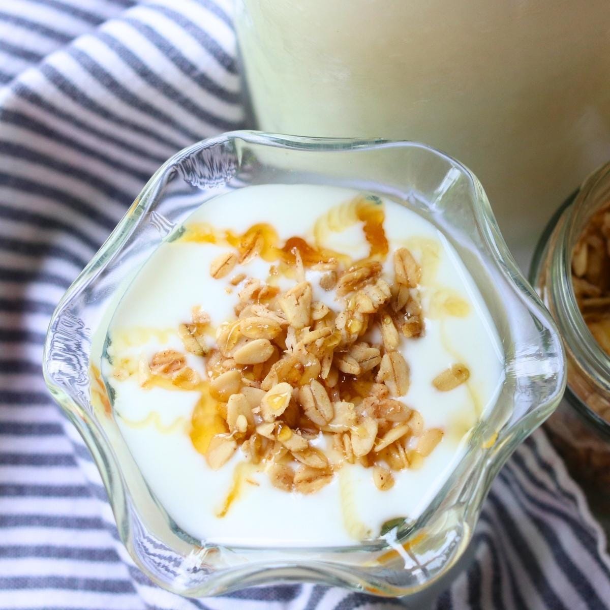 A glass dish of rich and creamy goat yogurt topped with granola and drizzled with honey. The setting is bright and inviting, evoking a fresh, healthy breakfast.