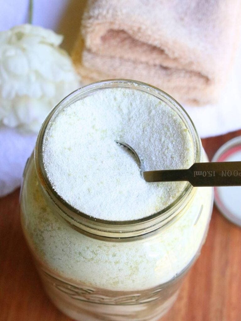 Tablespoon in a glass jar full of homemade laundry powder with clean towels in the background.