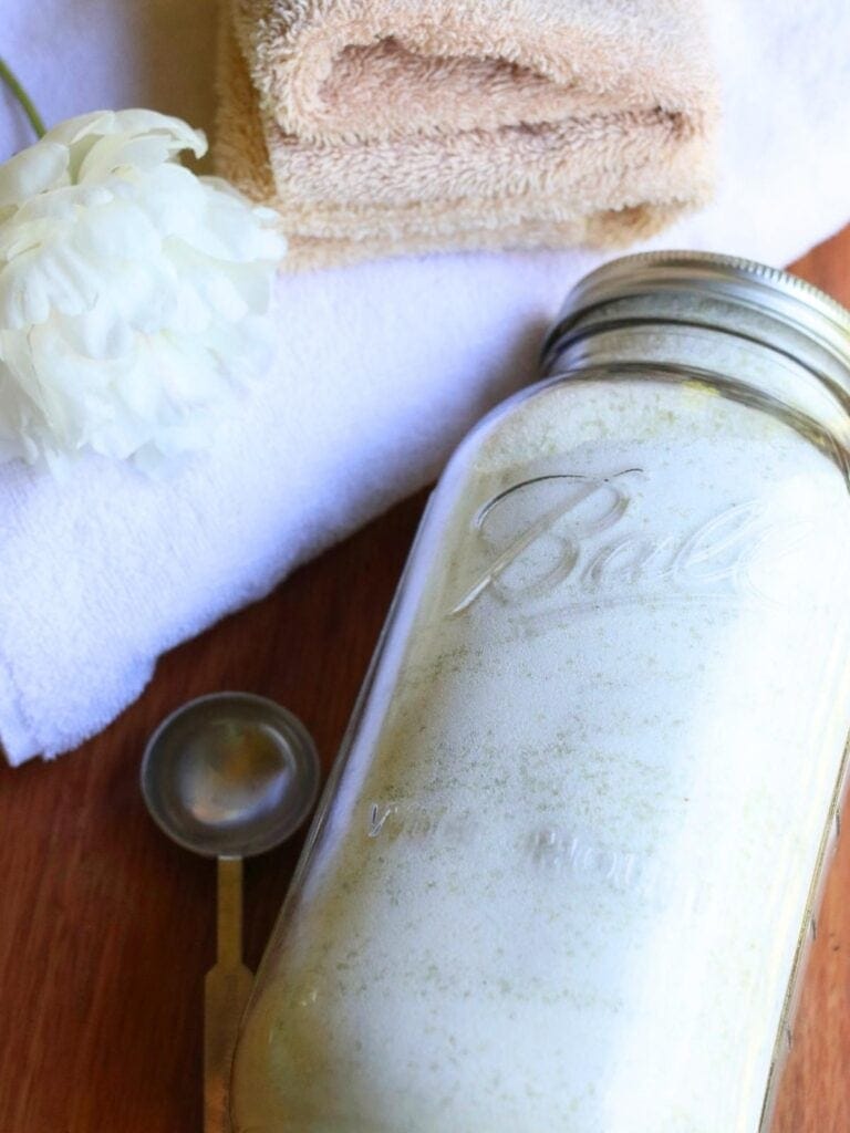 Glass jar full of homemade laundry powder on a wooden surface beside a stack of clean towels.