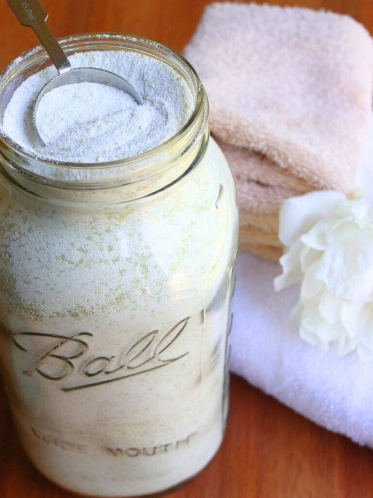 Tablespoon in a glass jar full of homemade laundry powder beside a stack of clean towels.