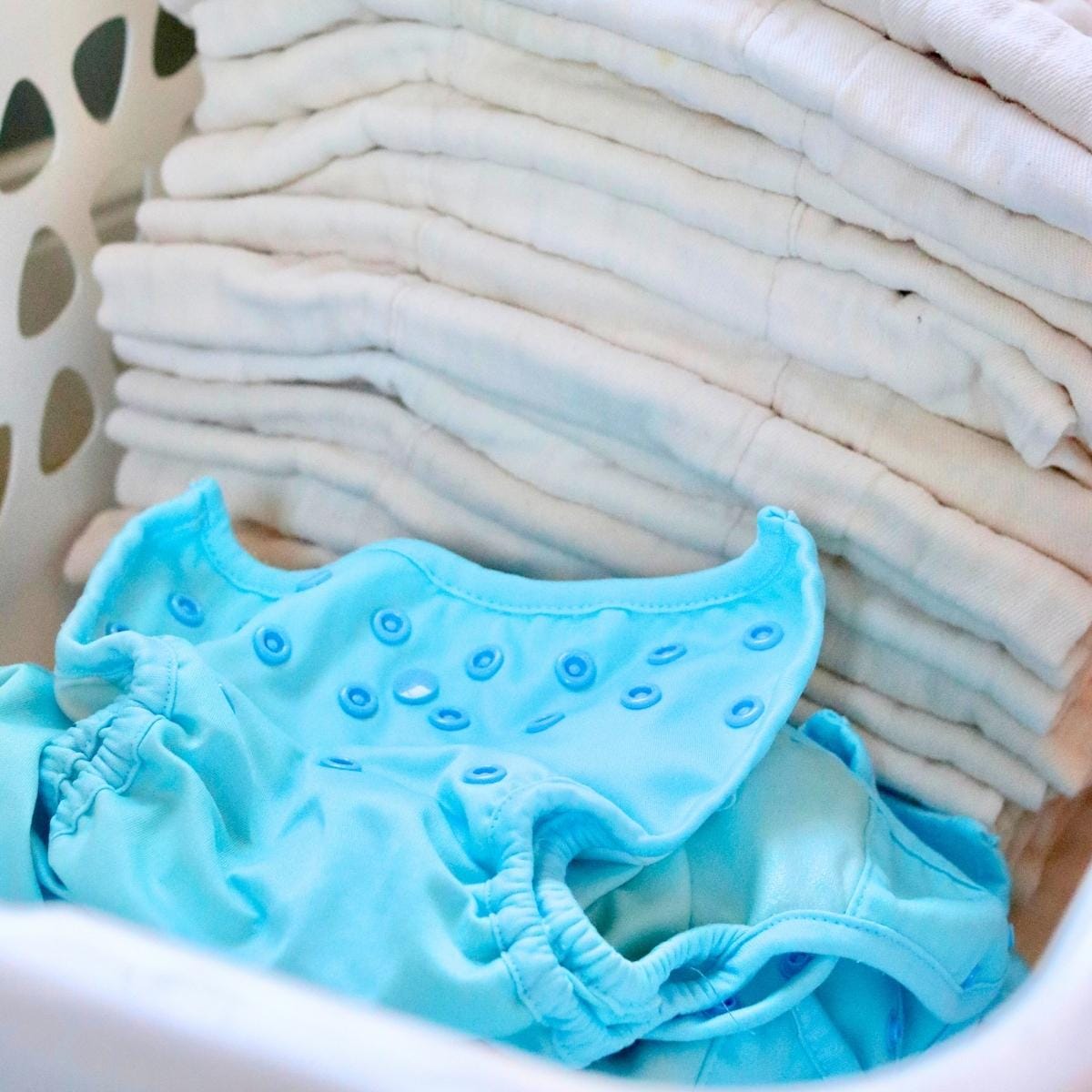 Reusable cloth diapers and blue diaper covers in a laundry basket – eco-friendly diapering solution for babies.