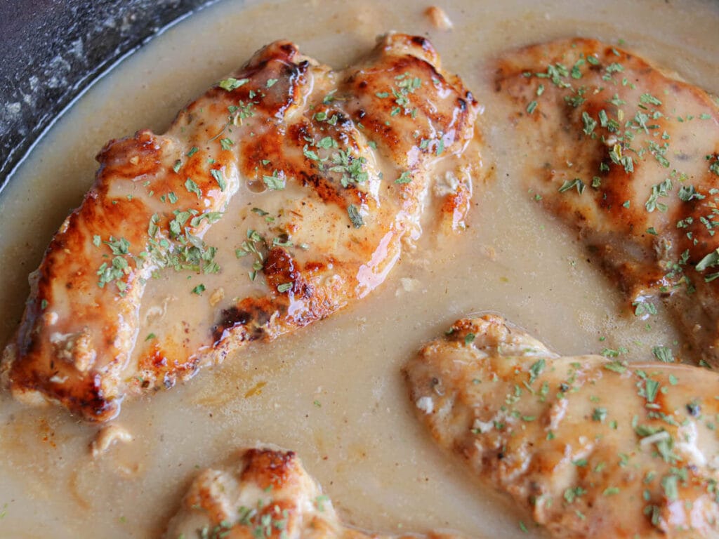 Close up of seasoned chicken breasts smothered in gravy in a cast iron skillet.