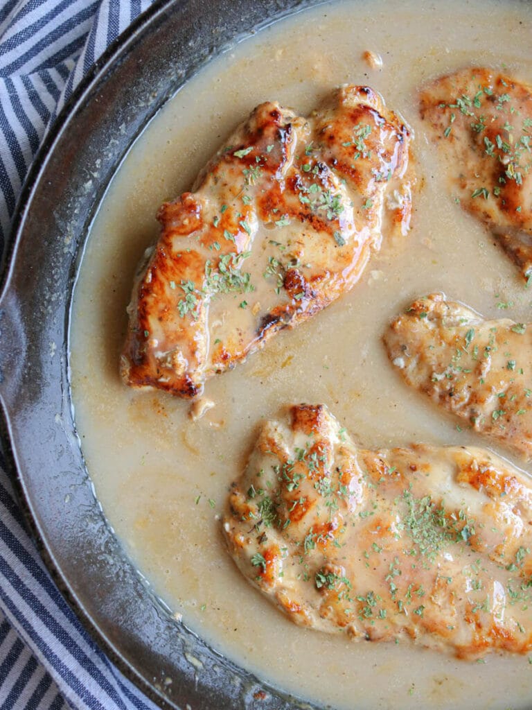 Seasoned chicken breasts in gravy in a cast iron skillet.
