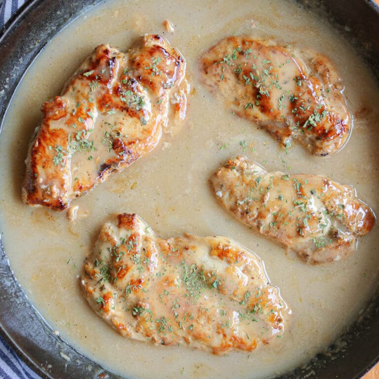 Four seasoned chicken breasts smothered in gravy in a cast iron skillet.