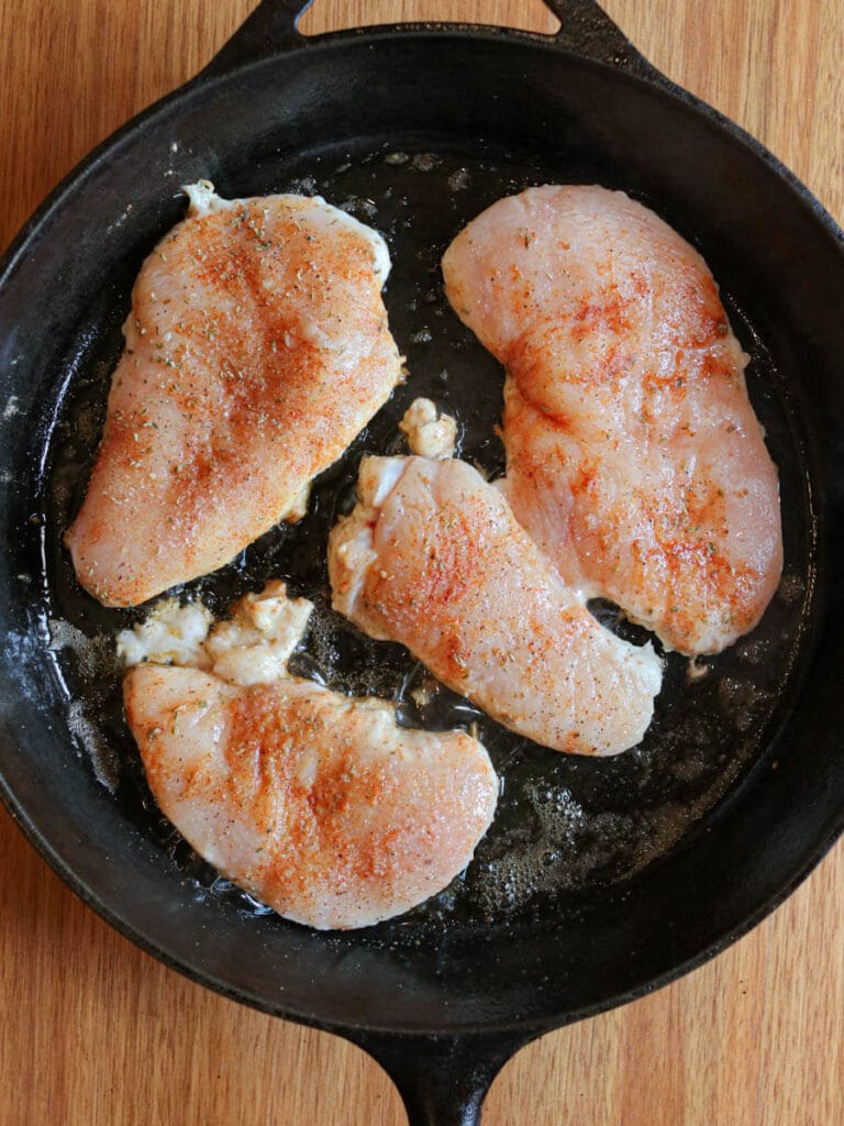 Cooking four seasoned chicken breasts in a cast iron skillet.