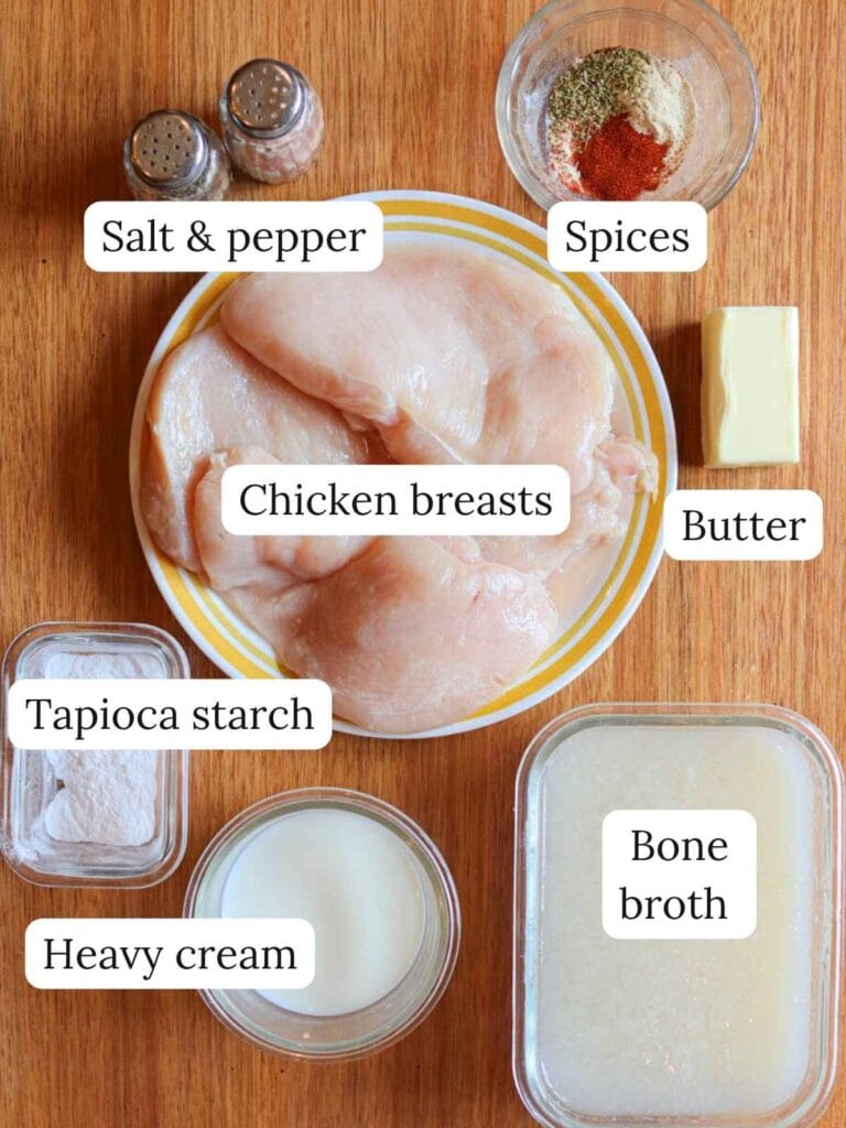 Labeled ingredients on a wooden table including salt, pepper, spices, chicken, butter, tapioca starch, heavy cream, and bone broth.