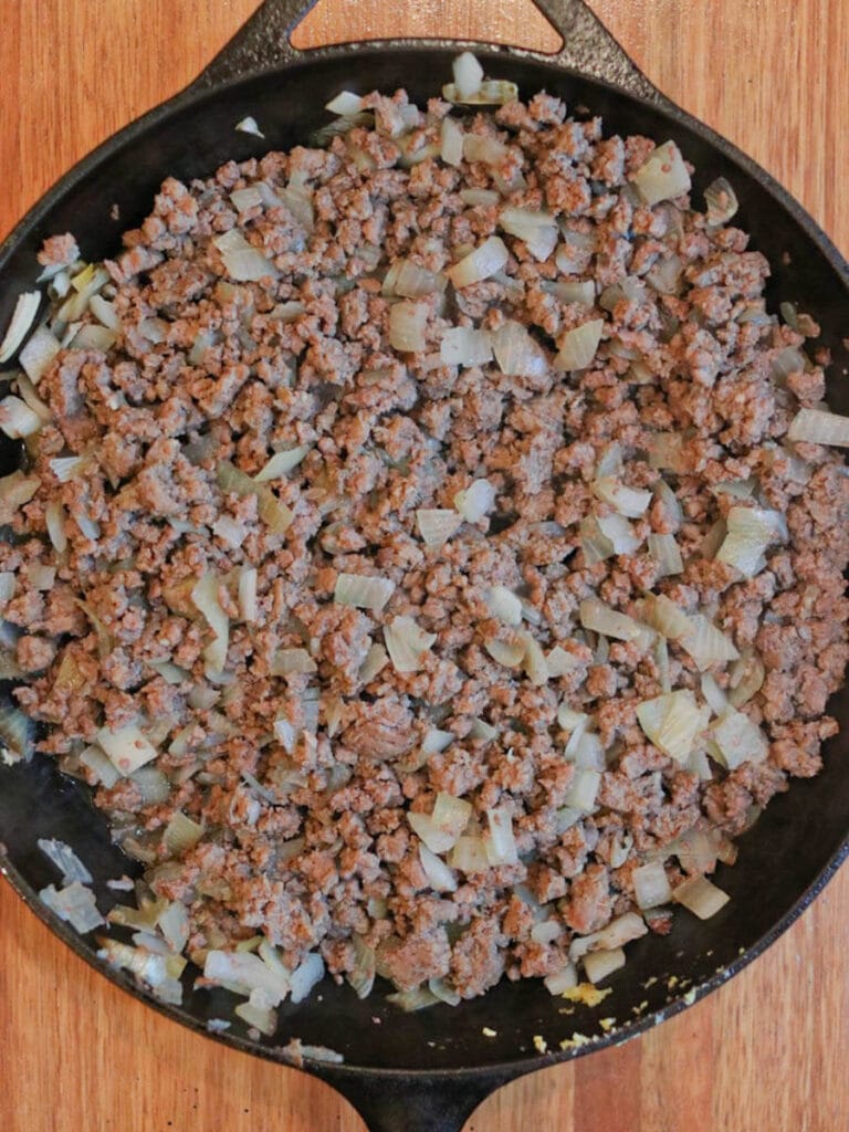 Cast iron skillet with ground beef and chopped onions on a wooden surface.