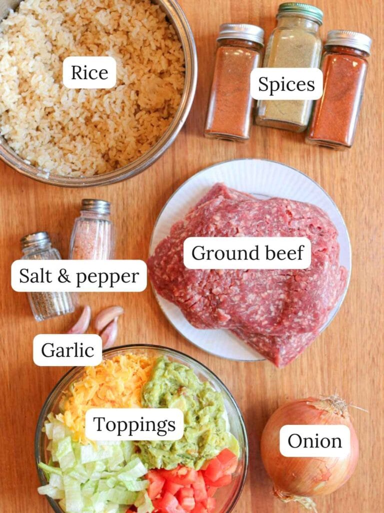 Labeled ingredients for ground beef rice bowls on a wooden background including rice, spices, salt, pepper, ground beef, garlic, toppings, and an onion.