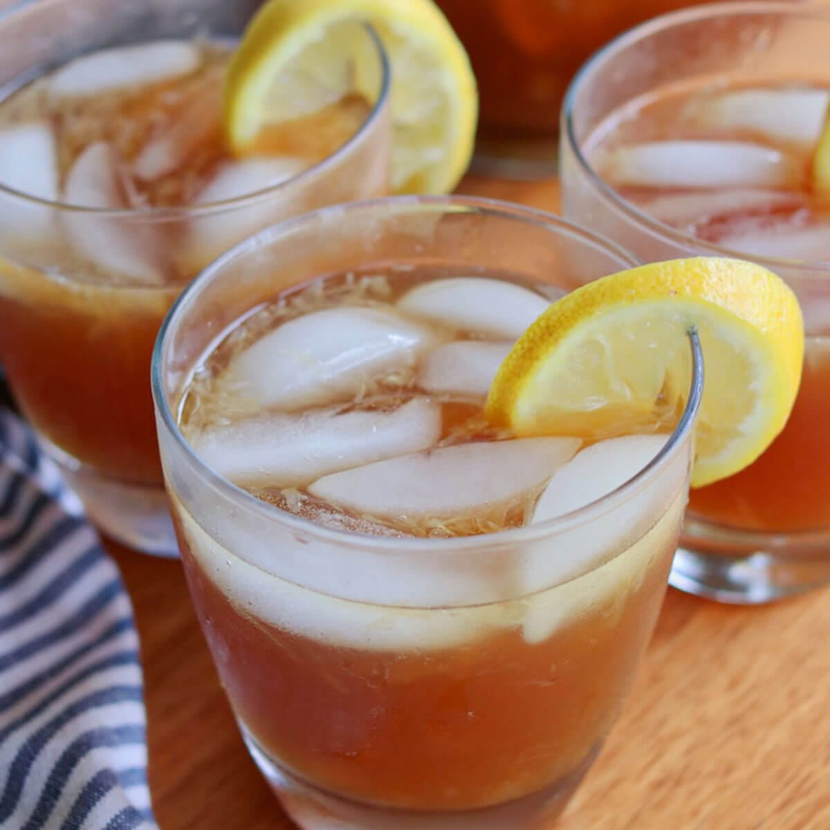 Close-up of three glasses filled with lemonade (healthy), garnished with lemon slices. The drinks sit on a wooden surface, next to a striped cloth napkin. Refreshing and inviting.