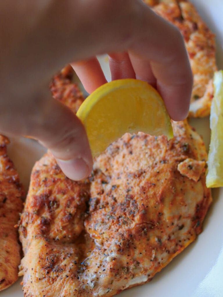 Hand squeezing fresh lemon juice over thin chicken.