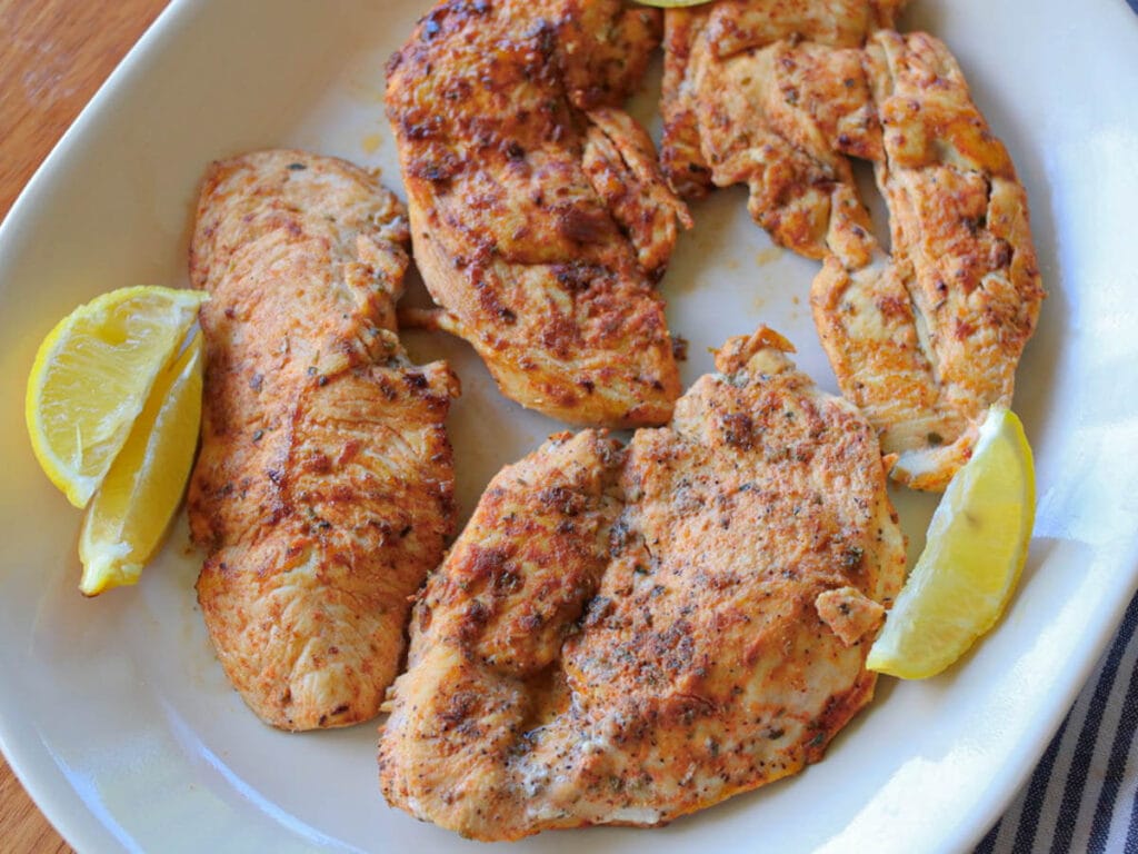 Closeup of white plate with four pieces of sliced chicken garnished with fresh lemon slices.
