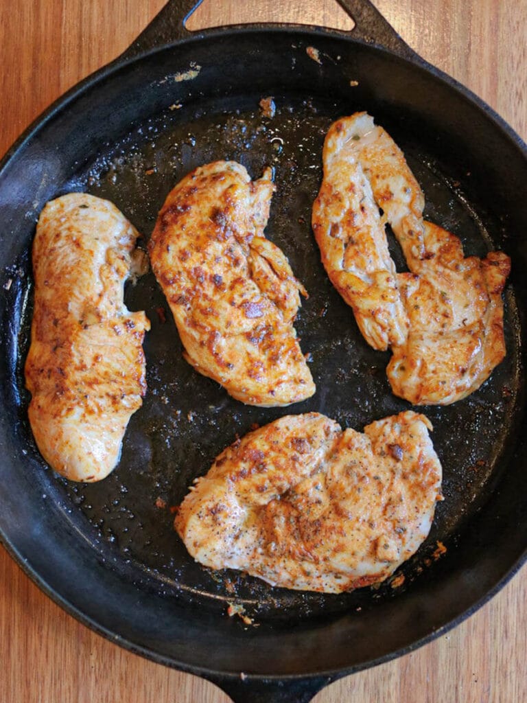 Thin cut chicken breasts cooking in butter in a cast iron skillet.