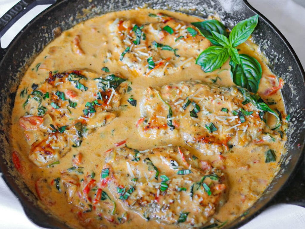 Tuscan chicken in a rich sauce garnished with fresh basil in a cast iron skillet.