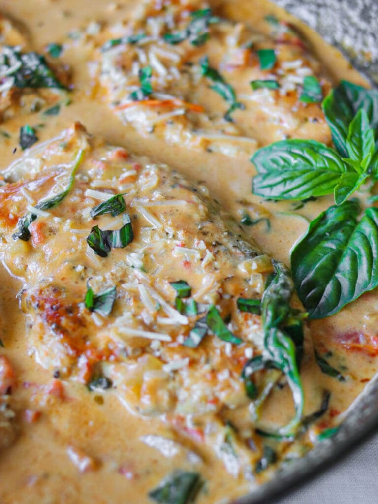 Close up of Tuscan chicken in a rich sauce garnished with fresh basil.