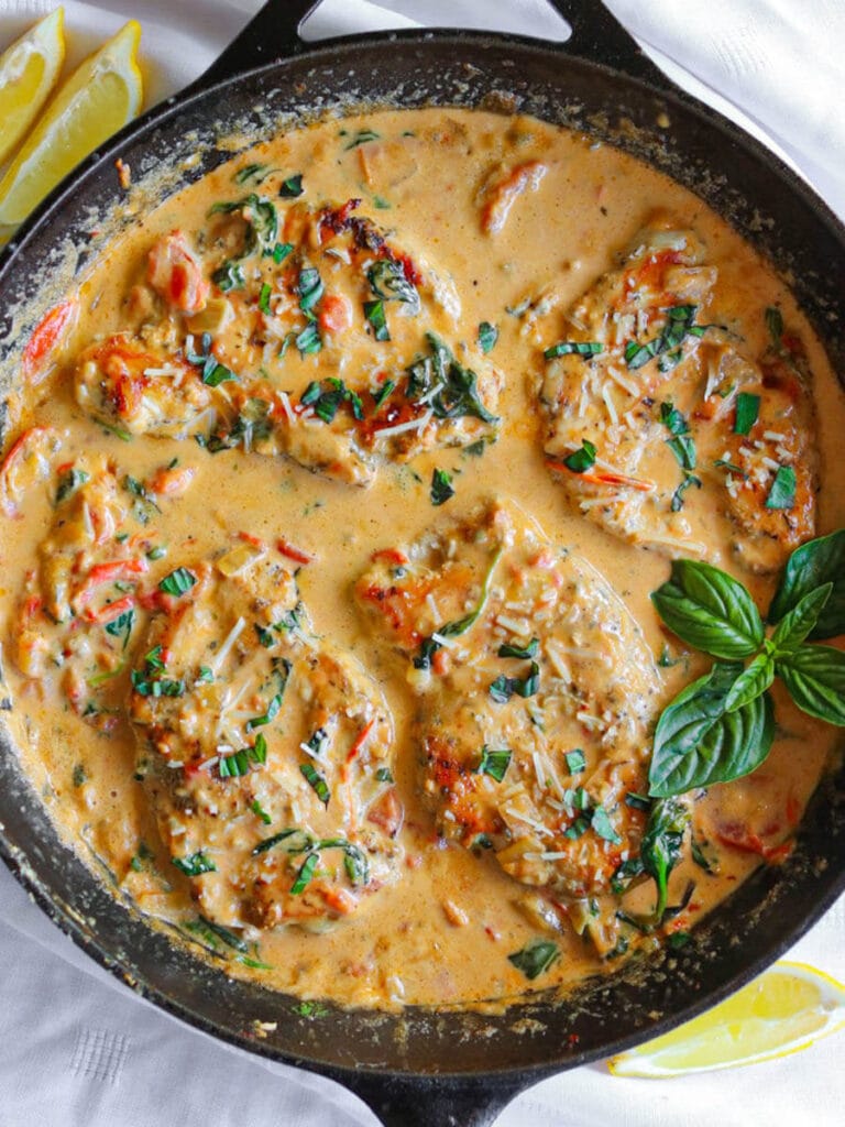 Top view of Tuscan chicken in a rich sauce garnished with fresh basil in a cast iron skillet with lemon slices on the side.