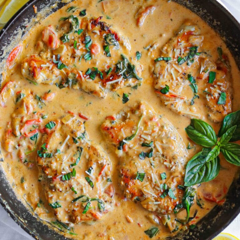 Top view of Tuscan chicken in a rich sauce garnished with fresh basil in a cast iron skillet.