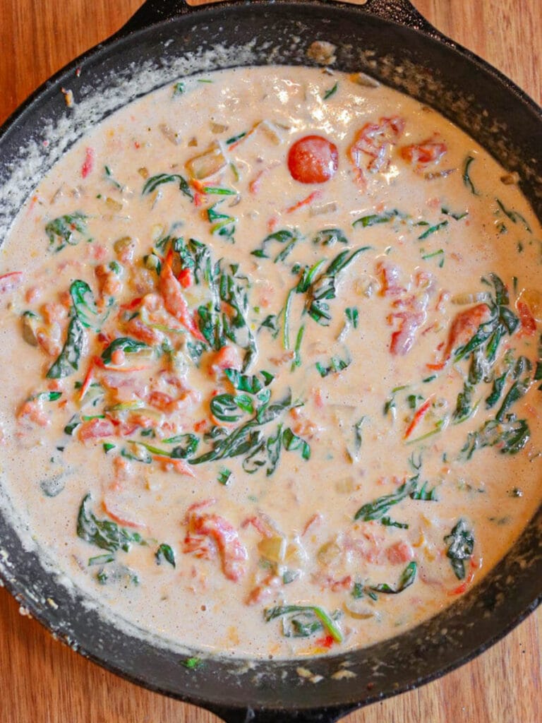 Creamy sauce with spinach and tomatoes in a cast iron skillet.