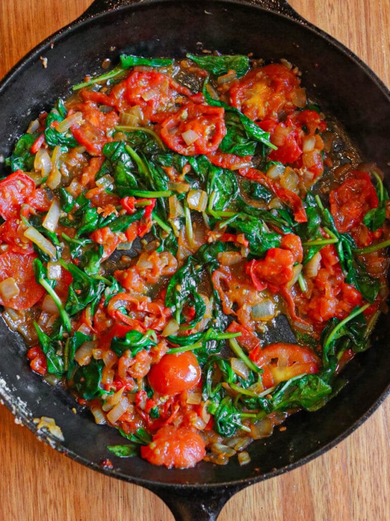 Cooking spinach and tomato slices in a cast iron skillet.