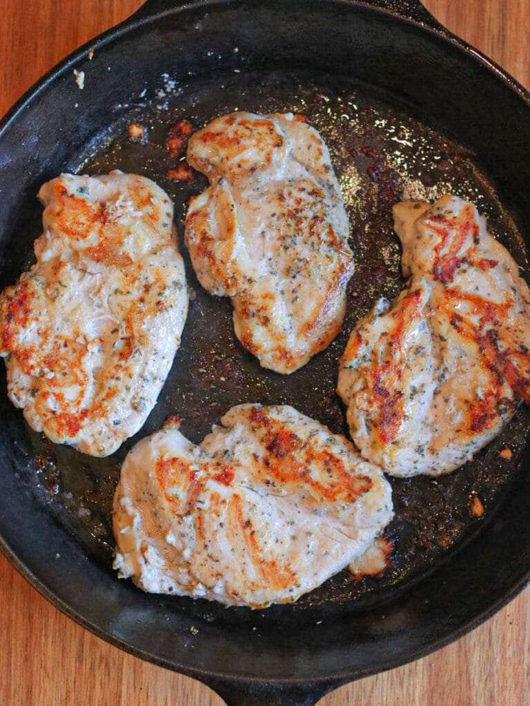 Four chicken breasts cooking in butter in a skillet.