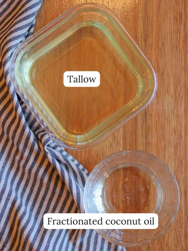 Labeled ingredients including melted tallow and fractionated coconut oil in glass containers on a wooden surface.