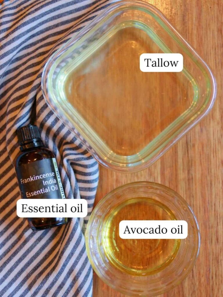 Labeled ingredients on a wooden table including tallow, essential oil, and avocado oil.