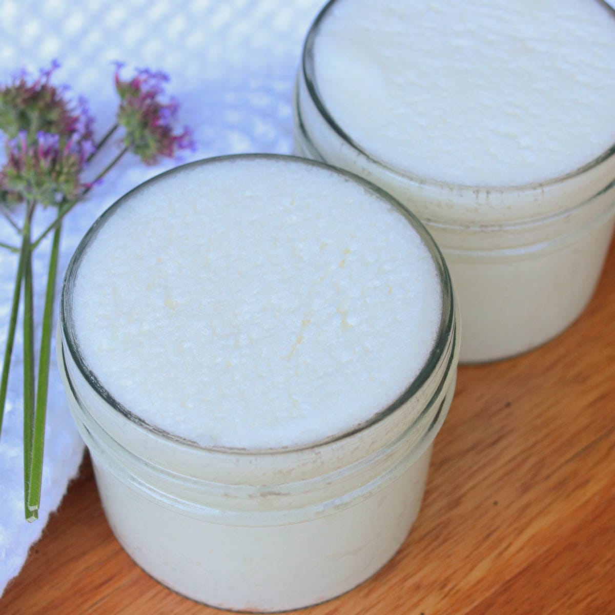 Glass jars with sugar scrub next to a white cloth and a sprig of fresh lavender.