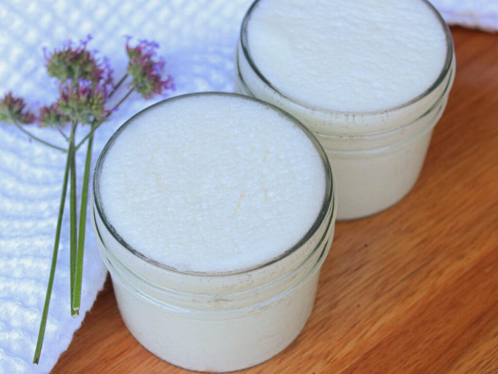 Two glass jars with homemade sugar scrub next to a white cloth and a sprig of fresh lavender.
