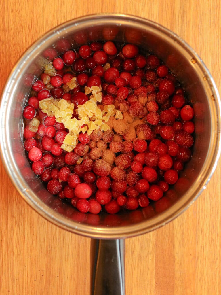 Ingredients for cranberry compote in a saucepan on a wooden surface.