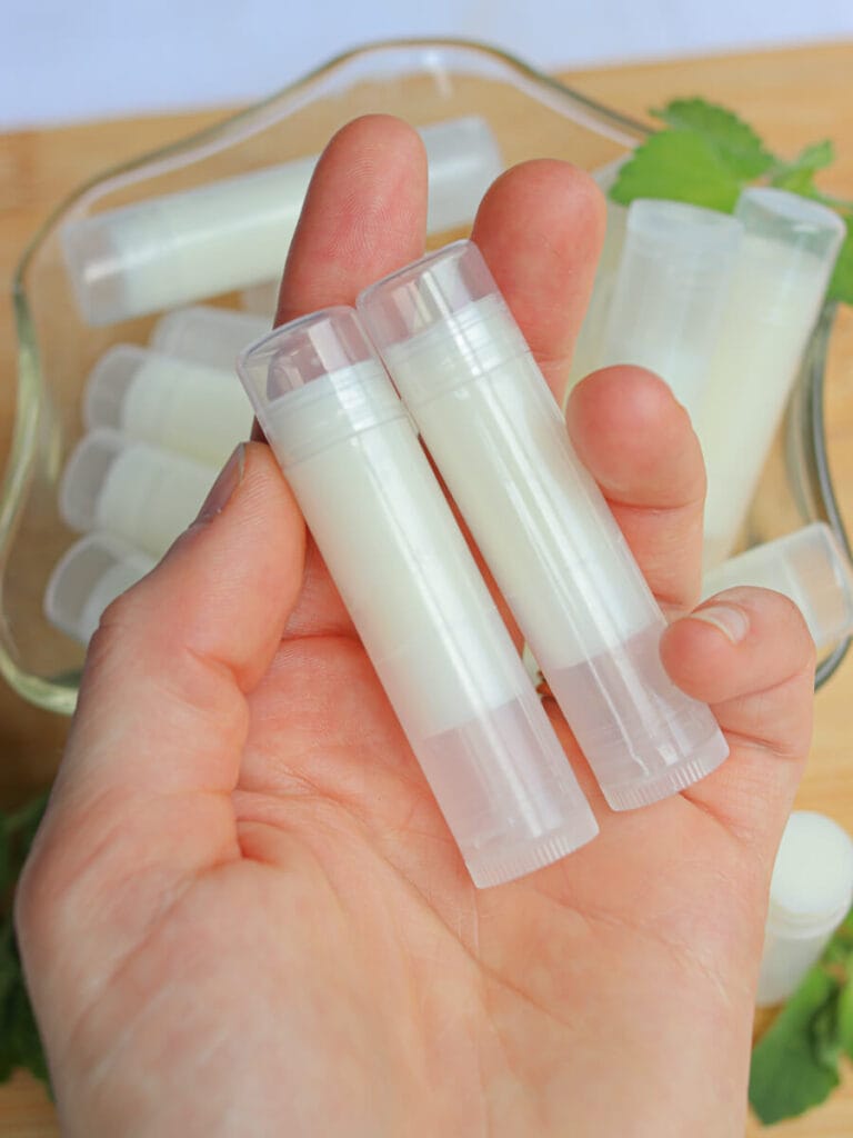 Hand holding two tubes of homemade lip balm.