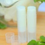 Closeup of two open tubes of lip balm on a wooden surface.