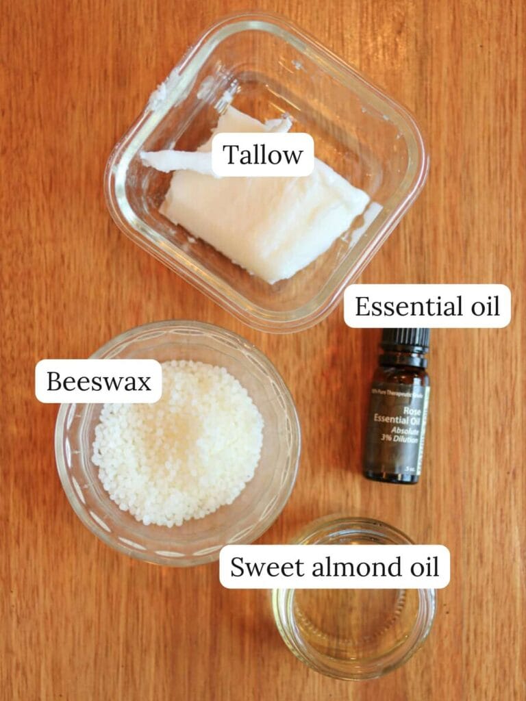 Labeled ingredients on a wooden table including tallow, beeswax, sweet almond oil, and essential oil.