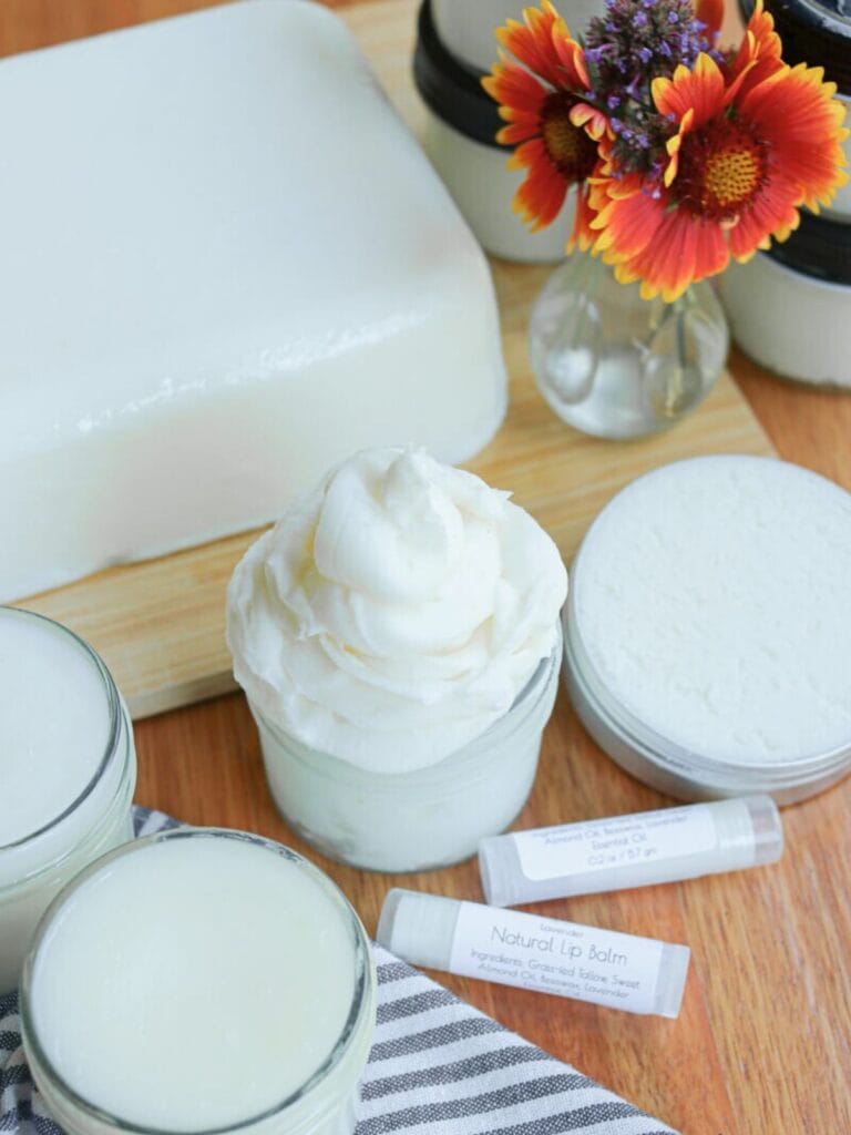 A block of tallow with various tallow skincare products beside a vase of fresh flowers.