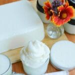 A block of tallow with various tallow products beside a vase of flowers.