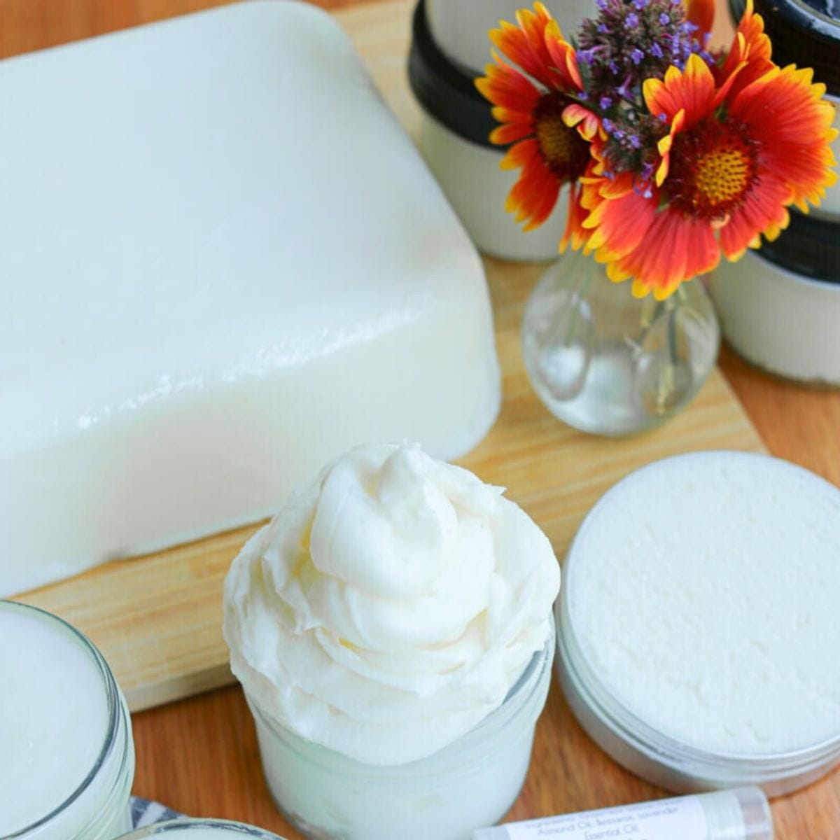 A block of tallow with various tallow products beside a vase of flowers.
