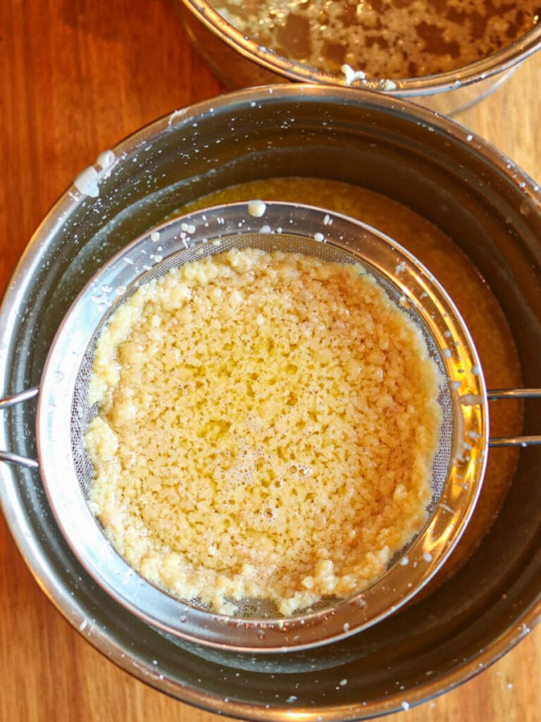 Straining melted tallow using a mesh strainer.