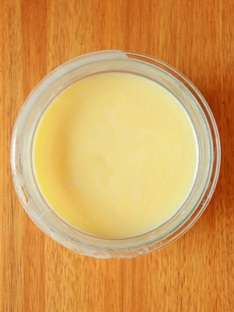 Tallow in a round glass container on a wooden surface.