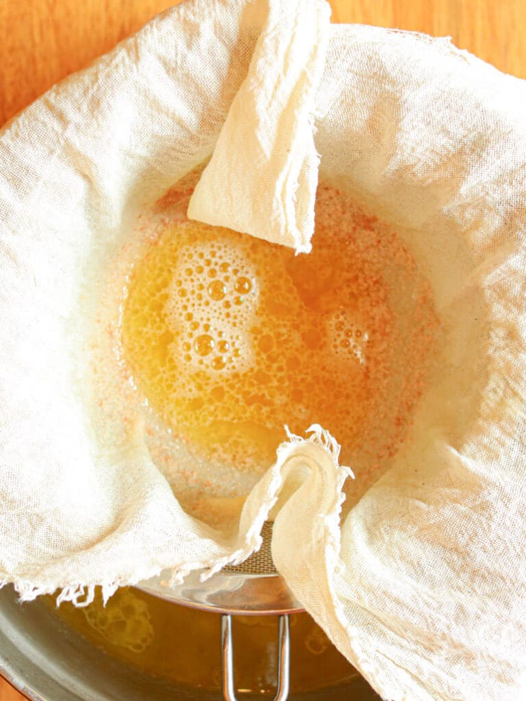 Straining melted tallow using a doubled cheesecloth.