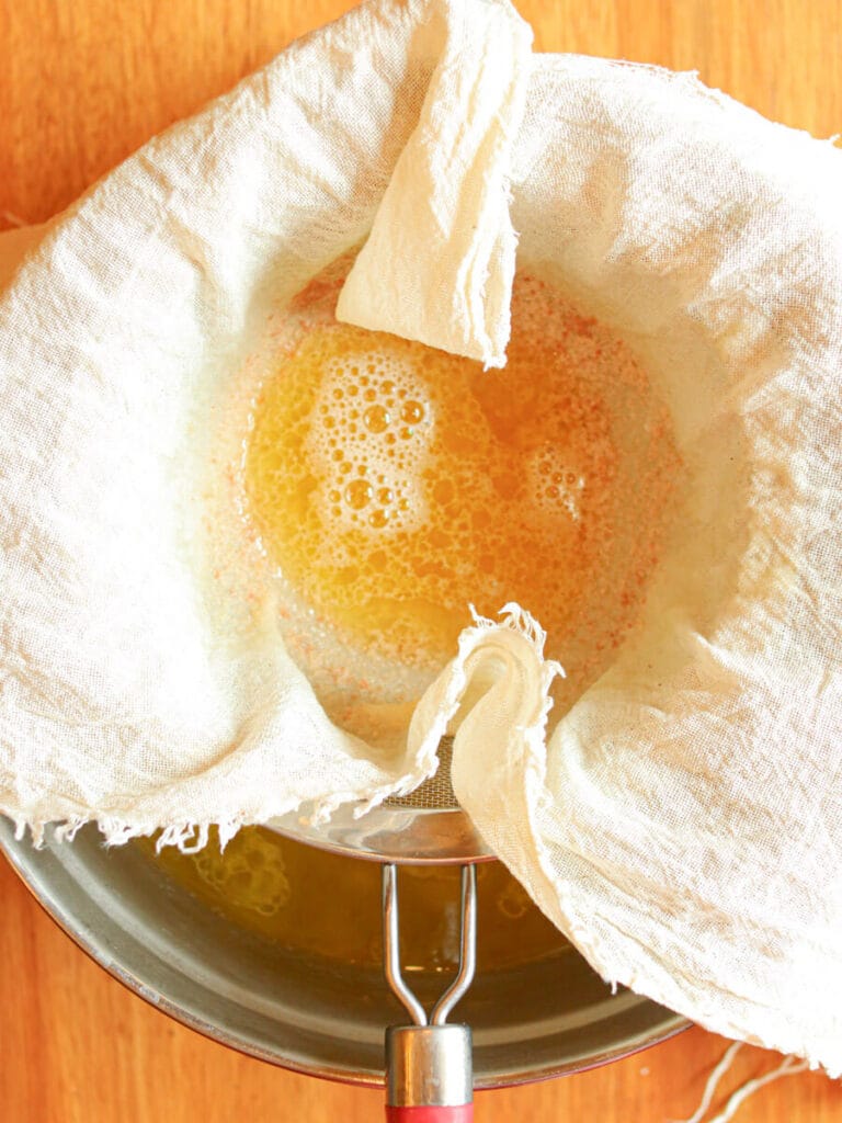 Straining melted tallow using a cheesecloth.