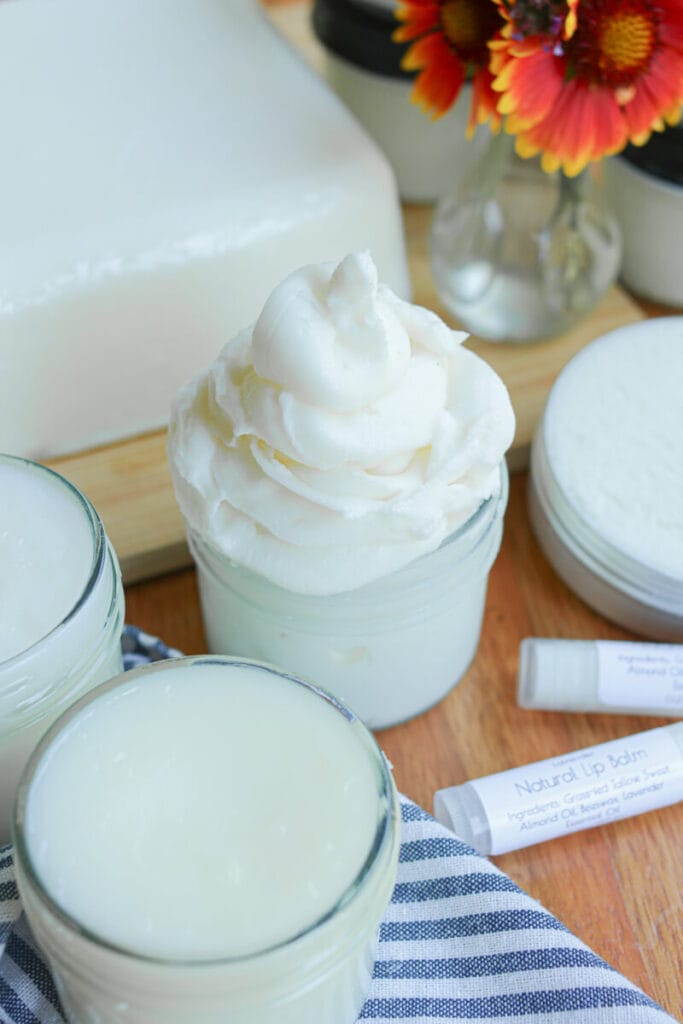 A block of tallow with tallow body butter, tallow balm, and other tallow skincare products on a wooden surface.