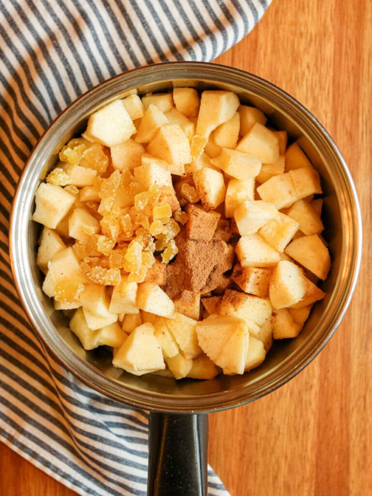 Chopped apples and other ingredients in a saucepan on a wooden surface.